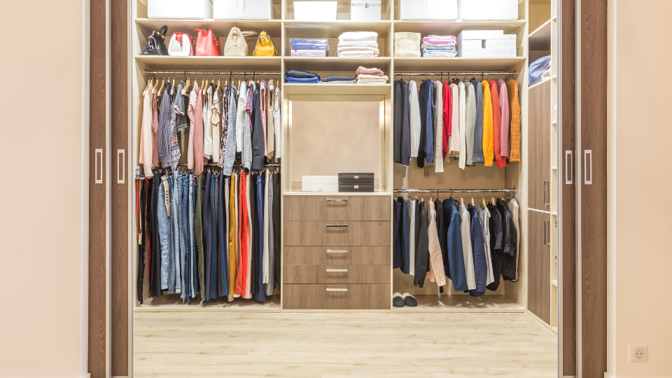 Modern wooden wardrobe with clothes hanging on rail in walk in closet